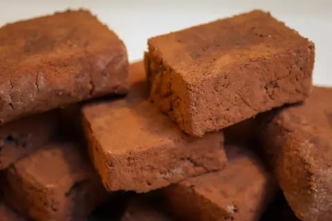 Stapel von schokoladigen Rohkost-Brownies, bestäubt mit Kakaopulver. Ein gesunder Genuss!