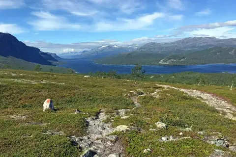 Vacker vy över en sjö och berg, med en stenröse markerad med rött. En vandringsled leder mot horisonten, kanske på väg mellan Kvikkjokk och Saltoluokta.
