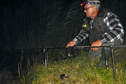 Ein Angler mit Stirnlampe prüft nachts seine John Sidley Rig-Ausrüstung am Ufer.