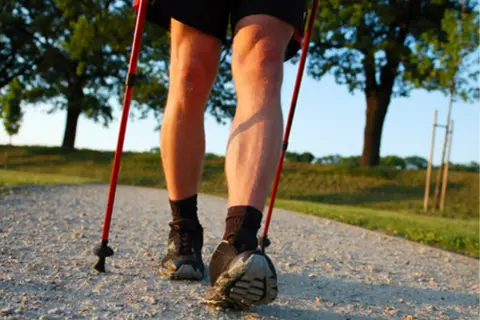 Nogi w butach i skarpetach, z kijkami nordic walking. Dowiedz się, jak prawidłowo założyć buciki na kijki nordic walking, by cieszyć się spacerem.