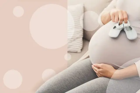 Ciężarna kobieta trzymająca małe buciki na brzuchu.