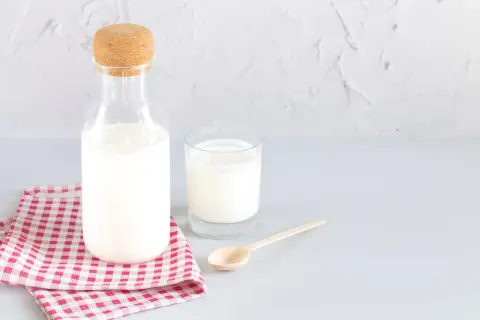 Bouteille de lait et verre sur une serviette à carreaux. Le lait battu, c'est quoi ? C'est ce lait frais et crémeux.