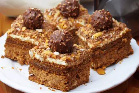 Pyszne ciasto Ferrero Rocher z kremem i orzechami, udekorowane całymi czekoladkami.