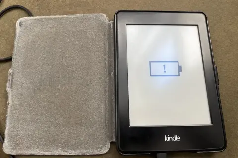 Un Kindle avec une batterie faible, prêt à être éteint. L'icône de batterie vide et le point d'exclamation indiquent qu'il est temps de le charger.