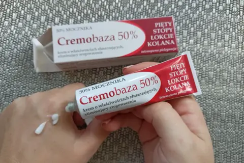Dłonie aplikują krem Cremobaza 50% na skórę, by wygładzić zrogowacenia na piętach, stopach, łokciach i kolanach.