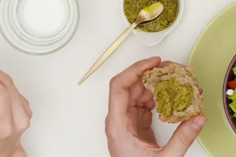 Main d'une personne tenant un morceau de pain avec du pesto, à côté d'une salade.