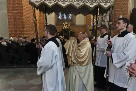 Uroczysta procesja w kościele, kapłan w złotej szacie niesie relikwie. To symboliczna rezurekcja.