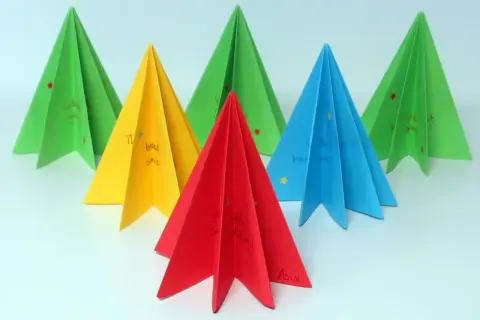 Kolorowe choinki origami płaskie z życzeniami. Zielone, żółte, czerwone i niebieskie ozdoby świąteczne.