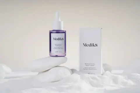 Serum Medik8 z bakuchiolem, roślinnym retinolem, na białych kamieniach i piasku.