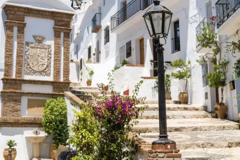 Escaleras empedradas y casas blancas adornadas con flores, un escudo de armas y una farola. Descubre qué ver en Frigiliana, un pueblo blanco andaluz.