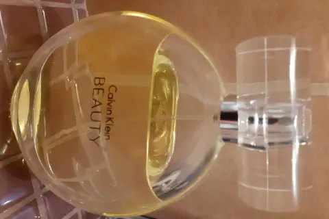 Flakon perfum Calvin Klein Beauty 100 ml, o bursztynowym kolorze, stoi na brązowym tle.