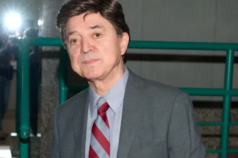 Jerzy Połomski w szarym garniturze i krawacie, otoczony przez błyski fleszy.