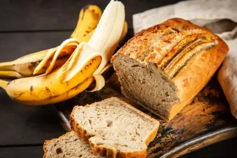 Wilgotne ciasto bananowe, obok dojrzałych bananów, kusi apetycznym wyglądem. Idealne na deser lub śniadanie.