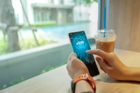 Dłoń trzyma smartfon z ikoną eSIM na ekranie, obok napoju.