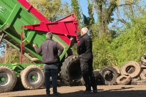 Deux hommes supervisent le déchargement d'une remorque verte remplie de pneus usagés, une étape clé du recyclage des pneus.