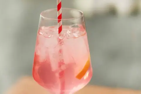 Erfrischender Sarti Spritz mit Eiswürfeln, einer Orangenscheibe und einem rot-weißen Strohhalm.