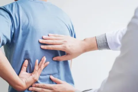 Dłoń terapeuty bada plecy pacjenta, szukając oznak bólu. Może to być wstęp do terapii, ale warto pamiętać o potencjalnych skutkach ubocznych nastawiania kręgosłupa.