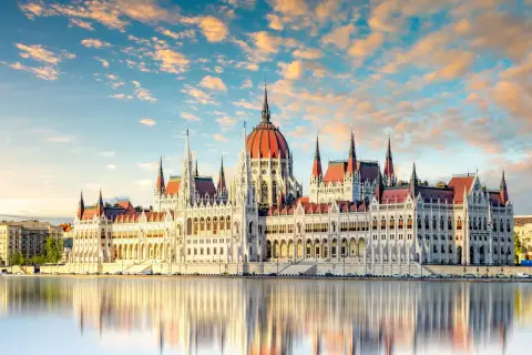 Budapeszt: Parlament odbija się w wodzie przy zachodzącym słońcu. Ceny noclegów i atrakcji są tu przystępne.