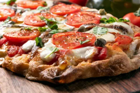 Knusprige Pizza mit Tomaten, Mozzarella und Basilikum auf einem Holzbrett.
