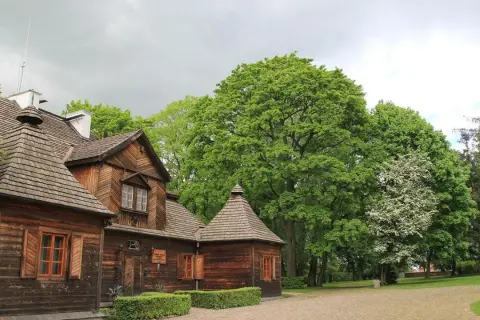 Drewniany dworek w Ożarowie koło Wielunia, otoczony bujną zielenią.