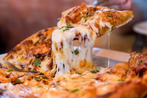 Ein Stück Pizza mit geschmolzenem Käse wird hochgehoben. Die vielen Pizza Kalorien sind es wert!