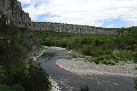 Rivière serpentant dans un cirque de falaises calcaires, le cirque de gens ruoms, bordé de verdure luxuriante.