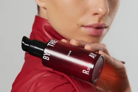 Kobieta w czerwonej ramonesce trzyma buteleczkę z serum. Czy to kwasy PHA jakie to? Delikatne dla skóry, dla blasku.