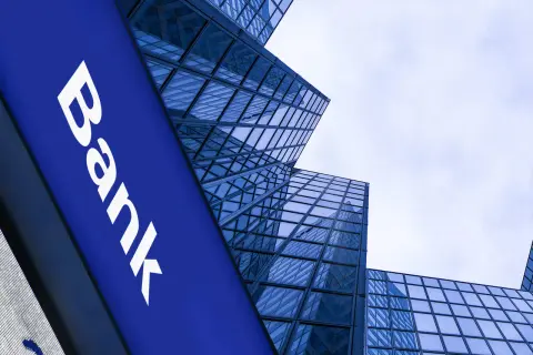 Niebieski szyld z napisem "Bank" na tle nowoczesnych, szklanych wieżowców. Czy to bank z 1600 roku?