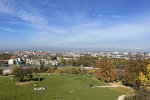 Jesienny dzień w Krakowie. Ludzie odpoczywają na zielonej trawie, a w tle rozciąga się panorama miasta.