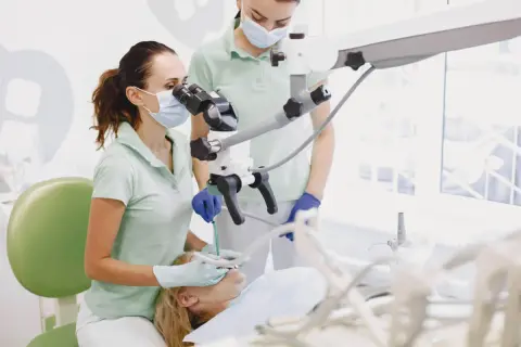 Dentystka z asystentką przy mikroskopie stomatologicznym, przygotowujące się do zabiegu, być może wyrywania ósemki.