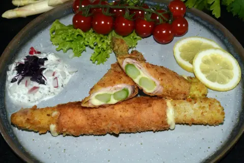 Knuspriges Spargel Cordon Bleu mit Schinken und Käse, serviert mit Dip, Tomaten und Zitrone.