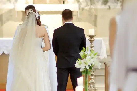 Para młoda podczas ceremonii ślubnej. W kościele panuje uroczysta atmosfera, a **limit osób na weselu** jest widoczny – obecni są tylko najbliżsi.