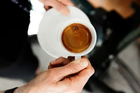 En hand håller en kopp med en perfekt dubbel espresso, med gyllene crema som lovar en intensiv smakupplevelse.