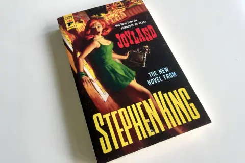 Bokomslaget till Stephen Kings "Joyland" med en skräckslagen kvinna i en grön klänning. En av många filmer med Stephen King som väntar på att bli sedd.
