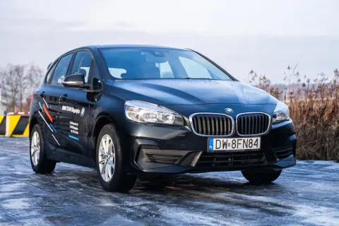 Ciemny BMW 218i na oblodzonej drodze, z logo BMW TEAM Długołęka na drzwiach.