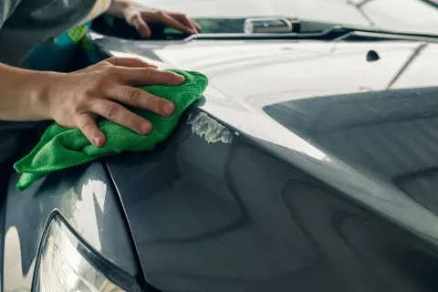 Manos puliendo el capó de un coche gris con un paño verde, mostrando cómo quitar arañazos del coche.