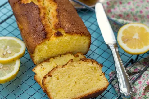 Un delicioso pastel de limón recién horneado, cortado en rebanadas y enfriándose en una rejilla, con rodajas de limón fresco al lado.