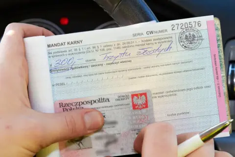 Ręce trzymają mandat karny na 300 zł. Wpisano "trzysta złotych", ale nie widać, ile punktów ma młody kierowca.
