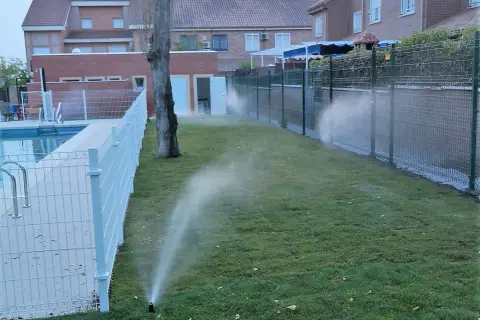 Aspersores riegan césped recién plantado junto a una piscina. Es el momento ideal para saber cuándo es mejor regar el césped y asegurar su crecimiento.