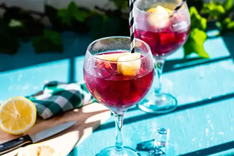 Två glas med tinto de verano, fyllda med is och citronklyftor, står på ett blått bord.