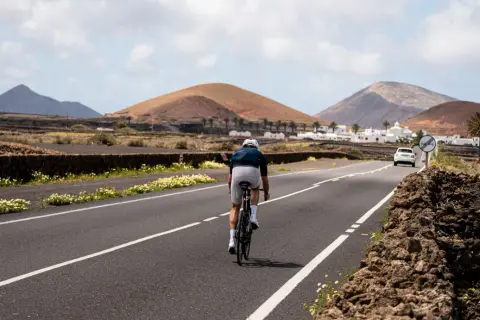 Ciclista pedaleando por una carretera en Lanzarote, rodeado de paisajes volcánicos y casas blancas. Una experiencia única de lanzarote en bici.