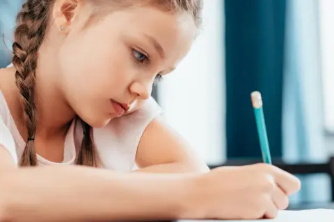 Bambina concentrata scrive con matita. Potrebbe essere una di quei bambini plusdotati 2 anni che già imparano a scrivere.