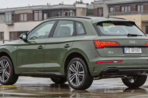 Zielony q5 audi na mokrym parkingu, w tle budynki.