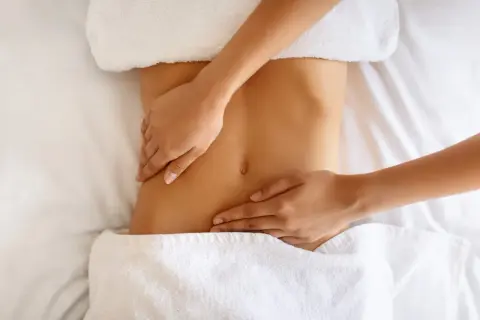 Hände massieren sanft den Bauch einer Frau. Manche empfinden Lymphdrainage als schmerzhaft, doch hier scheint es eine wohltuende Behandlung zu sein.
