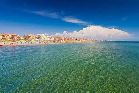 Słoneczny dzień nad morzem w Rzymie. Tłumy plażowiczów, kolorowe parasole i budynki wzdłuż wybrzeża.