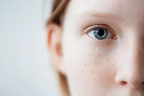 Nahaufnahme eines blauen Auges und der Wange einer Person mit Sommersprossen. Sanfte Pflege für empfindliche Haut ist hier sichtbar.