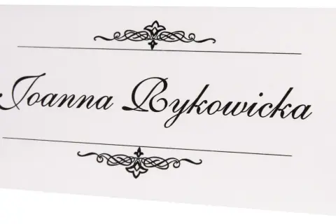 Elegancka winietka z imieniem "Joanna Bykowicz" ozdobiona ornamentami. Idealna inspiracja, jak zrobić winietki na przyjęcie.