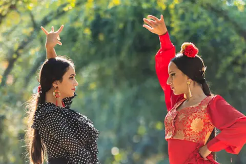 Dos bailarinas de un grupo flamenco famoso, con trajes vibrantes, ejecutan pasos elegantes bajo la luz del sol.