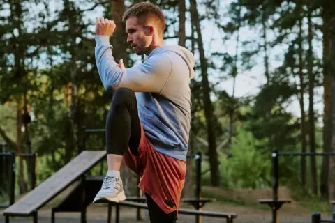 Mann im Freien beim **hit training**, hebt ein Knie, konzentriert sich auf seine Bewegung.