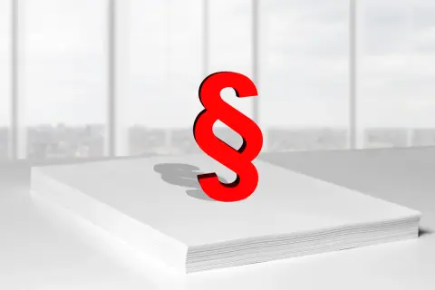 Czerwony znak paragrafu na stercie białych kartek symbolizuje zwięzłe omówienie ustawy o finansach publicznych.